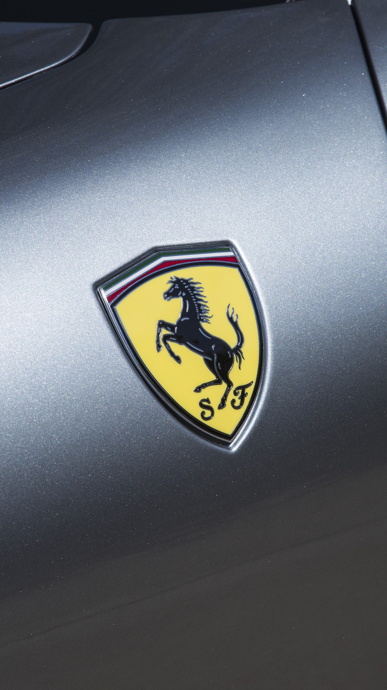 Yellow Ferrari badge against a metallic silver hood